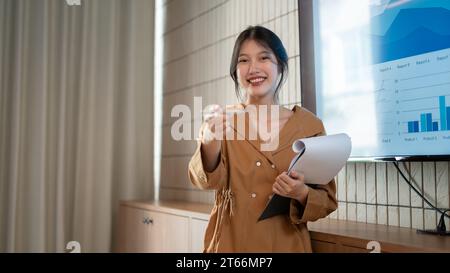 Una giovane donna d'affari asiatica bella e sicura di sé lascia che chiunque all'incontro le faccia una domanda durante la sua presentazione all'incontro. Foto Stock