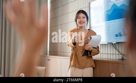 Una giovane donna d'affari asiatica bella e sicura di sé lascia che chiunque all'incontro le faccia una domanda durante la sua presentazione all'incontro. Foto Stock