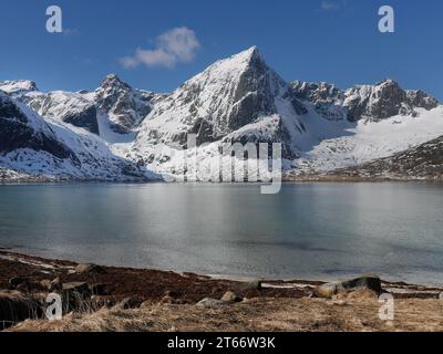 Respirate la splendida cima della montagna Stortind e i laghi della baia Flakstadpollen, Flakstadøy, Lofoten, la natura norvegese, la neve invernale contro il cielo blu, Turquo Foto Stock