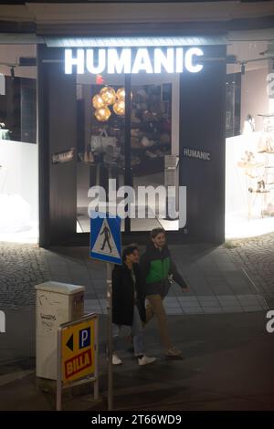 Due uomini camminano di fronte al negozio Humanic, Vienna Austria di notte in inverno, fotografati da un alto edificio Foto Stock