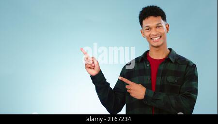 Ritratto, sorriso e uomo con la mano che punta allo studio per il mockup, lo spazio o le notizie su sfondo blu. Presentazione, sorriso e volto del modello Foto Stock