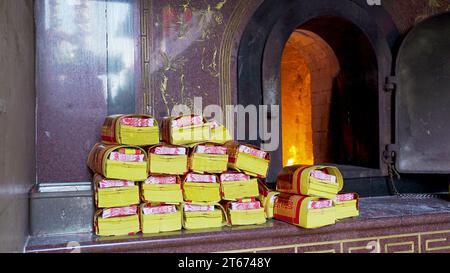 Soldi dello spirito d'oro impilati dal bruciatore, in attesa del rogo ritualistico. Carta di Joss, carta di incenso, soldi di carta, soldi fantasma, offrire soldi Foto Stock