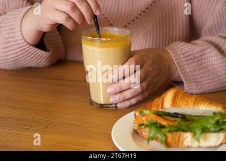 Donna in un accogliente pullover caldo che regge una tazza di caffè. Bevanda piccante sana curcuma autunnale. Latte di zucca con Curcuma nelle mani femminili da vicino. IO Foto Stock