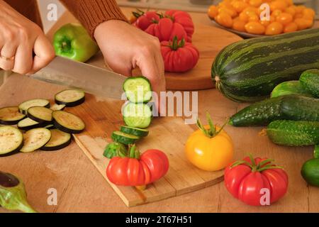 Pomodori grandi maturi, melanzane, verdure su un locale di lavoro in legno della cucina. Molte verdure crude di fondo. Pomodoro, cetrioli. Fornello a casa che fa una h Foto Stock