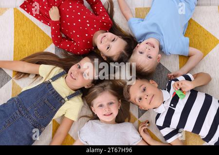 Adorabili bambini sdraiati su un tappeto luminoso insieme all'asilo, vista dall'alto. Attività di gioco Foto Stock