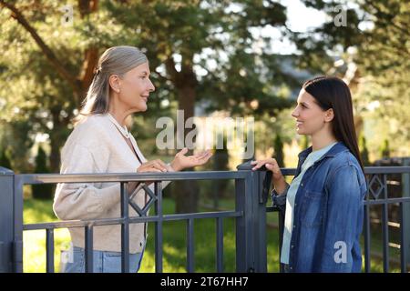 Rapporto amichevole con i vicini. Donne felici che parlano vicino alla recinzione all'aperto Foto Stock