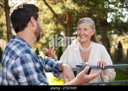 Rapporto amichevole con i vicini. Donna anziana felice che parla con un uomo vicino alla recinzione all'aperto Foto Stock