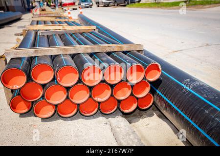 Confezione di nuovi tubi dell'acqua in plastica impilati sulla strada, pronti per essere collocati in trincea in cantiere. Foto Stock