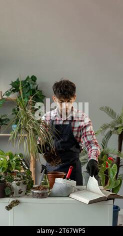 Un giovane arabo che lavora nel giardino di casa leggendo un vecchio libro. Trapiantando in un nuovo vaso da fiori, il fioraio ama l'hobby Foto Stock