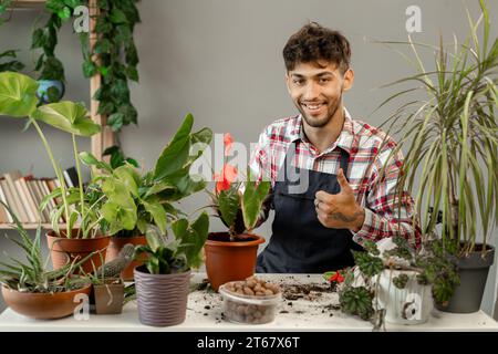 Un uomo arabo sorridente che trasporta piante verdi a casa. Felice giardiniere maschio o fiorista si prendono cura dei fiori domestici. Concetto di giardinaggio. Foto Stock