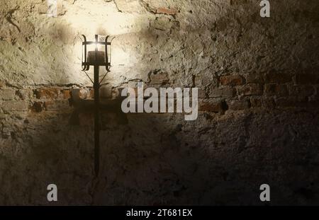 Torcia del castello medievale illuminata appesa a un muro di pietra, oggetti d'epoca e sfondo Foto Stock