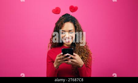 Giovane donna carina vestita per San Valentino con l'app per appuntamenti, cellulare, studio Foto Stock