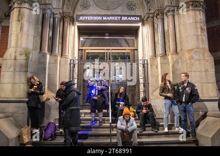 Un gruppo di persone diverse in piedi di notte sui gradini di un edificio, con bagagli e altri oggetti personali nelle vicinanze Foto Stock