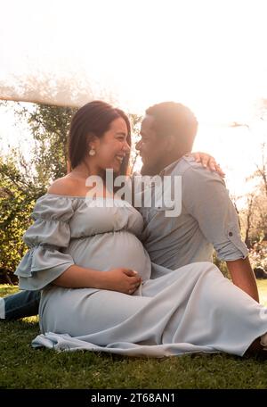 Una donna latina incinta e una coppia di uomini africani seduti in un lussureggiante parco illuminato dal sole Foto Stock