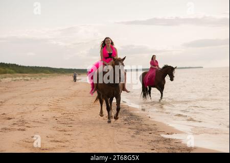 Una vista mozzafiato di una donna in un vestito rosa che cavalca un cavallo lungo una spiaggia Foto Stock
