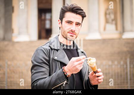 Un uomo con una giacca di pelle tiene un gelato o un cono gelato Foto Stock