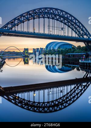Il Tyne Bridge si riflette nel fiume Tyne all'alba con lo spettacolare Millenium Bridge e il Sage Center sullo sfondo Foto Stock