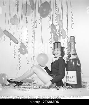 Champagne negli anni '1950 Una giovane donna in una scena che chiaramente dovrebbe suggerire qualcosa da festeggiare. Una bottiglia gigante di champagne Delck fa parte dell'arredamento, palloncini e coriandoli appesi sullo sfondo. Svezia 1952 rif. BK82-6 Foto Stock