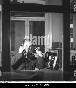 La telefonia negli anni '1940 Un uomo a un centralino telefonico. Collega le chiamate in entrata e in uscita alla persona giusta utilizzando i cavi per i rispettivi telefoni in un centralino telefonico. Sembra felice di essere al lavoro, sorridendo a parlare su due telefoni contemporaneamente. Svezia 1945 Kristoffersson rif O149-3 Foto Stock