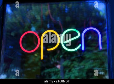 Cartello al neon con scritta "Open" con lettere di colori diversi. Finestrino anteriore. Foto Stock