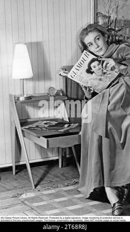 Negli anni '1950 Una donna si vede leggere una rivista in qualche modo seduta su un letto con una madia di legno visibile. Svezia 1957 Foto Stock