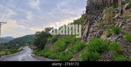 Un paesaggio naturale panoramico caratterizzato da una formazione rocciosa situata lungo una strada, con uno sfondo di linee elettriche Foto Stock