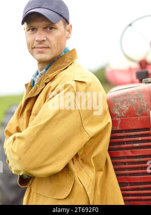 Vi aiuto a procurarvi frutta e verdura - Farmer. Ritratto di un contadino con le braccia incrociate appoggiandosi al cofano del trattore. Foto Stock
