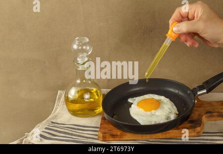 donna che frigge un uovo, versando olio d'oliva con contagocce a causa del prezzo eccessivo dell'olio , concetto di aumento dei prezzi Foto Stock