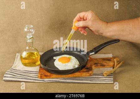 donna che frigge a mano un uovo, versando olio d'oliva con contagocce a causa del prezzo eccessivo dell'olio , concetto di aumento del prezzo Foto Stock