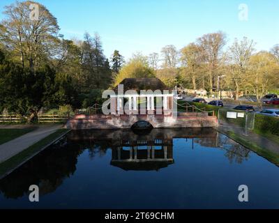 Una scena idilliaca caratterizzata da un pittoresco ponte in legno che si arrocca su un tranquillo stagno in un tranquillo parco, con un pittoresco gazebo nel Foto Stock