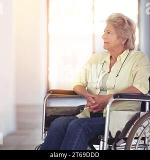 Sto facendo un viaggio nella corsia dei ricordi. una donna anziana che sembra premurosa mentre è seduta su una sedia a rotelle a casa. Foto Stock