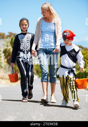 Fare scherzi o dolcetti. Bambini in costume che vanno a fare una cura o a fare una cura con la loro mamma. Foto Stock