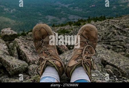 Piedi in vecchi scarponi da trekking marroni su uno sfondo roccioso e boscoso. viaggiate in montagna. dettagli delle scarpe da viaggio Foto Stock