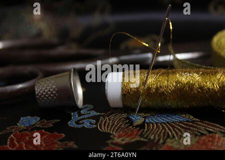 Rocchetto di filo d'oro con ditale su tessuto di seta asiatica nera Foto Stock