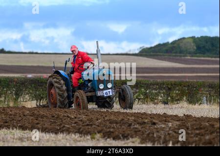 Un agricoltore sta utilizzando un trattore rosso in un vasto campo agricolo aperto Foto Stock