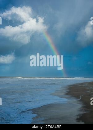 Uno splendido paesaggio di una spiaggia con un arcobaleno che si innalza sull'oceano in una luminosa giornata di sole Foto Stock