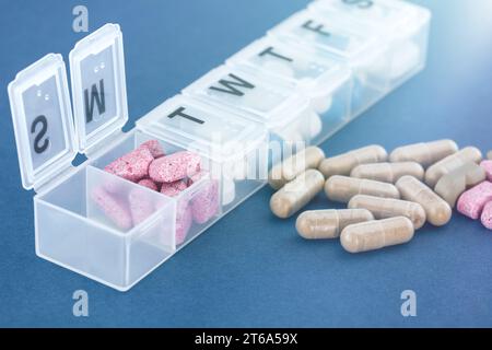 Una settimana di farmaci in una scatola di pillole bianche e accanto in una pila su un tavolo blu. Foto Stock