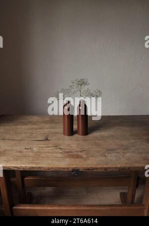 Composizione artistica minimalista. Frammenti di un'antica casa di campagna all'interno - pareti intonacate illuminate, un antico tavolo in legno, bottiglie smaltate in argilla Foto Stock