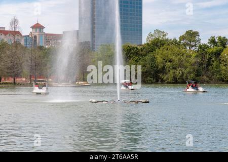 Giovani famiglie che pilotano pedalò intorno alla fontana sul lago McGovern all'Hermann Park nel centro di Houston, Texas Foto Stock