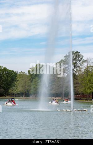 Giovani famiglie che pilotano pedalò intorno alla fontana sul lago McGovern all'Hermann Park nel centro di Houston, Texas Foto Stock