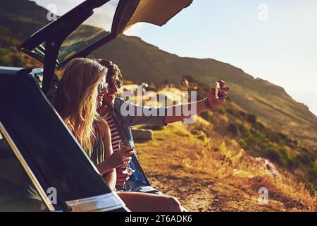 Roadtrip. una giovane coppia felice che posa per un selfie con la sua auto in un viaggio in macchina. Foto Stock