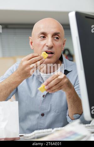 uomo che mangia patatine davanti al computer Foto Stock