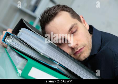 uomo stanco che dorme su una cartella con documenti Foto Stock