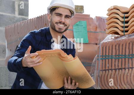 giovane muratore barbuto che prende mattoni rossi dalla pila Foto Stock