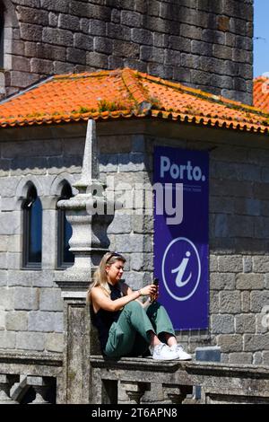 Una turista guarda il suo smartphone davanti all'ufficio dell'Associazione Turistica di Porto, Terreiro da sé Terrace, Porto / Oporto, Portogallo Foto Stock