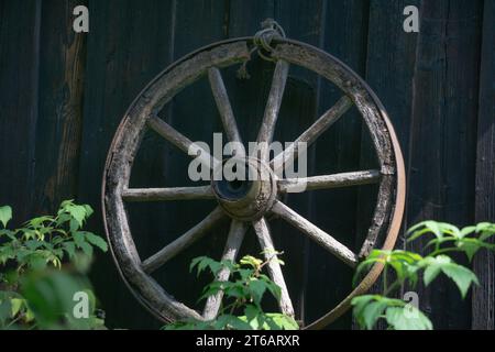 Una vecchia ruota di legno in una treccia di ferro sulla parete di una casa Foto Stock