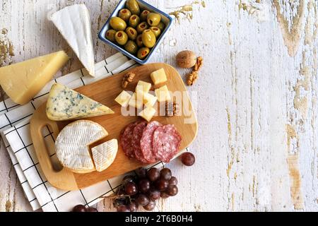 Diversi tipi di formaggi con uva, olive e noci su fondo bianco Foto Stock