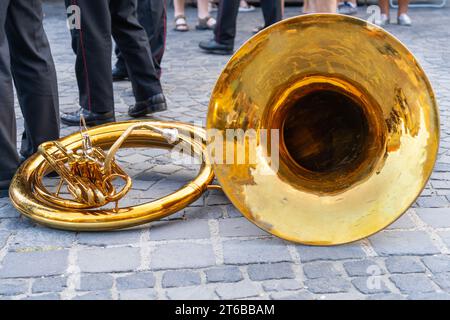 Tuba di ottone che giace per terra in una strada acciottolata con musicisti soldato sullo sfondo Foto Stock