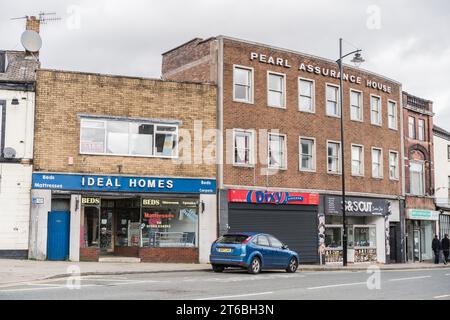 Burslem, Stoke on Trent, Inghilterra, 21 marzo 2023. Auto blu parcheggiata sulla strada principale con un negozio di materassi, piatti da asporto con pollo fritto e negozio di barbieri. Foto Stock