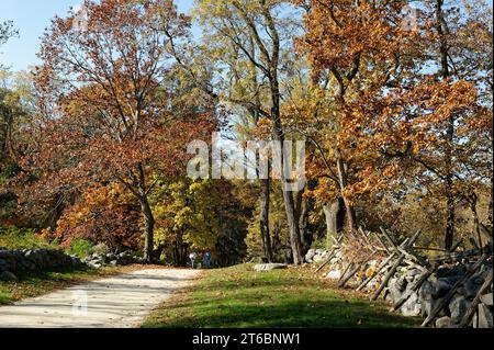 Ottobre 2023 Battle Road - Lincoln, Massachusetts. I turisti camminano lungo una strada sterrata in direzione della storica Hartwell Tavern in un autunno colorato Foto Stock